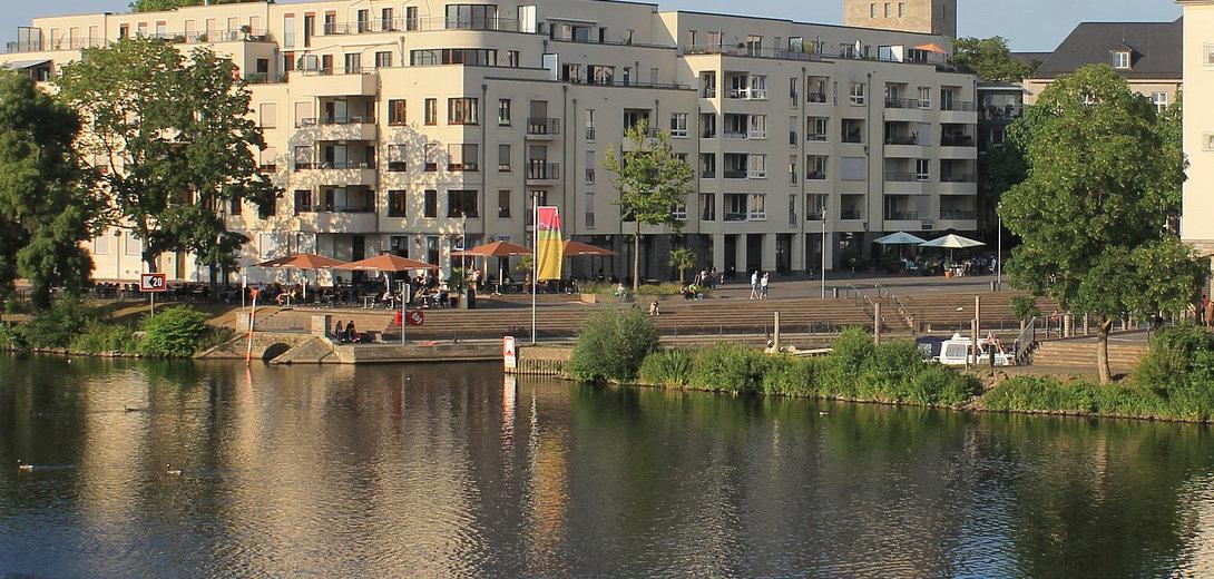 Ein Gebäudeensemble aus Turm und Rathaus am Ufer des Ruhr-Flusses mit Spiegelung in ruhigem Gewässer