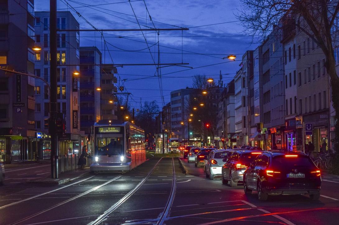 Abendlicher Straßenverkehr in Düsseldorf mit Straßenbahn und Autos im Stadtzentrum.